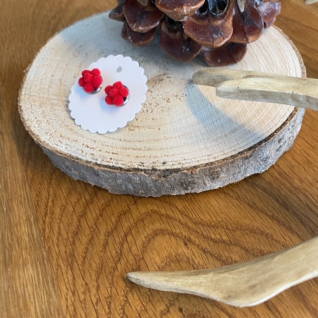 Bollenhut Ohrringe in Blumenform, handgefertigt im Schwarzwald, auf weißer Karte – präsentiert auf Holzscheibe mit Kiefernzapfen und Geweihdeko.