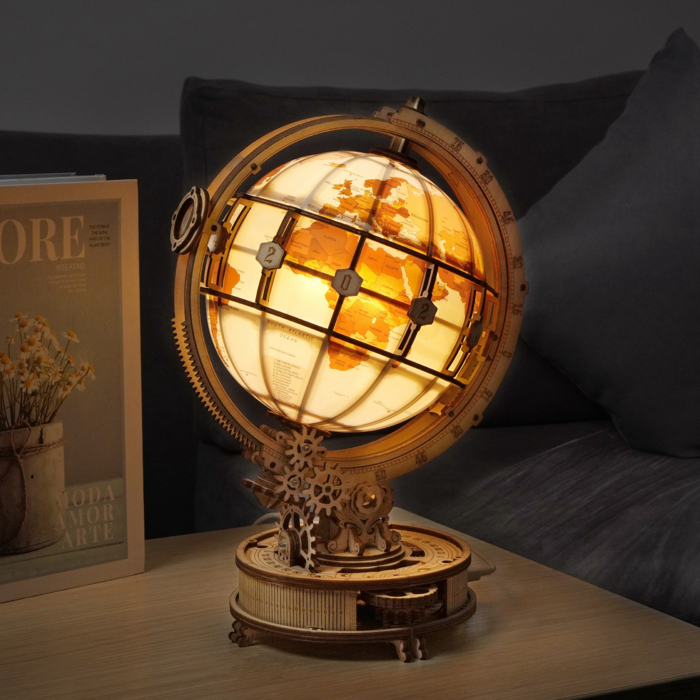 Ein 3D-Holzpuzzle Globus, beleuchtet, gefertigt mit CO2-Laserschneidetechnologie und Zahnrädern, steht auf einem Tisch neben einer Zeitschrift und einem dunklen Sofa.