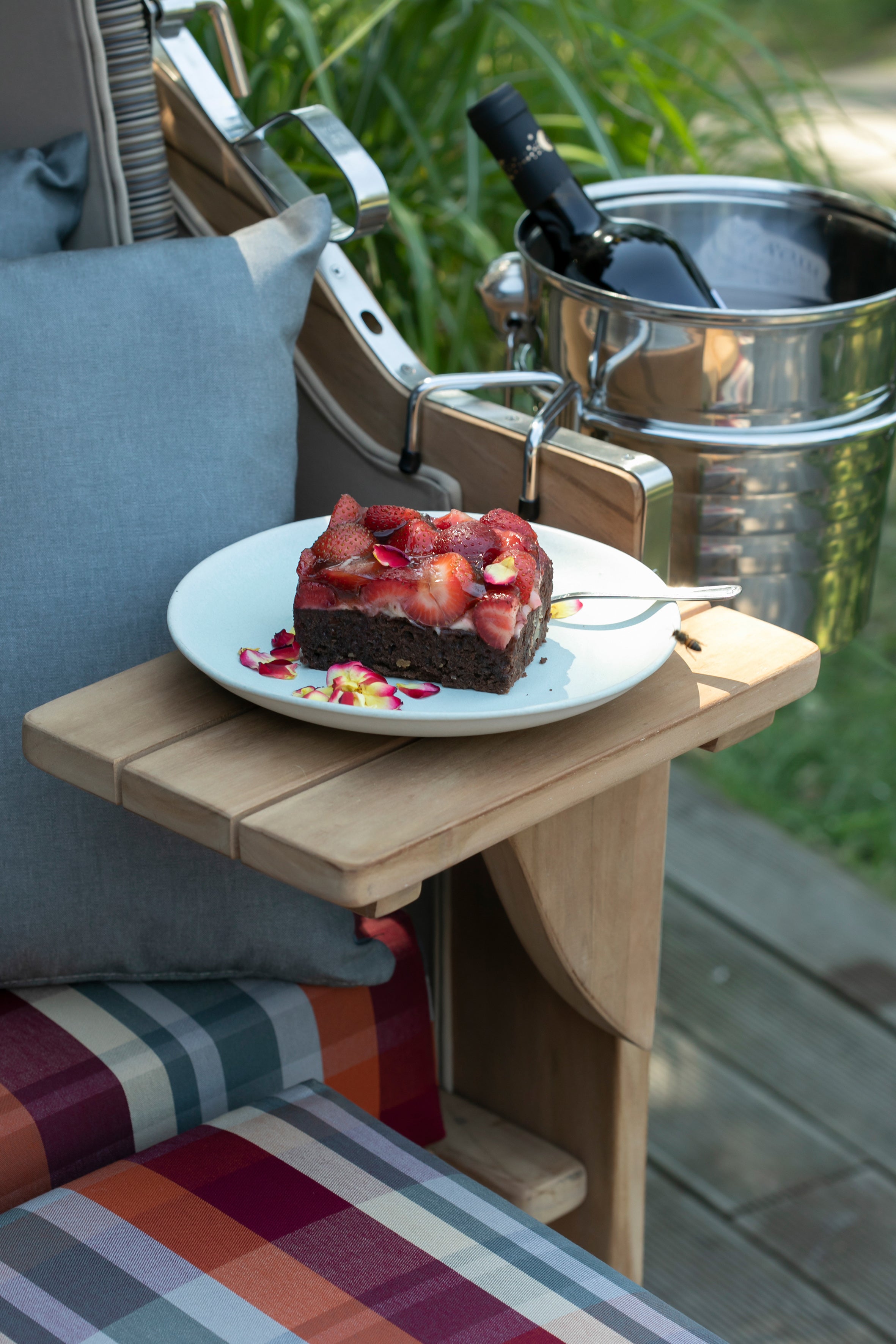 Ein Teller mit Schokoladenkuchen und Erdbeeren steht auf einem Holztablett im Freien neben dem Strandkorb-Getränkekühler und verleiht Ihrem Genuss im Freien den perfekten luxuriösen Touch.