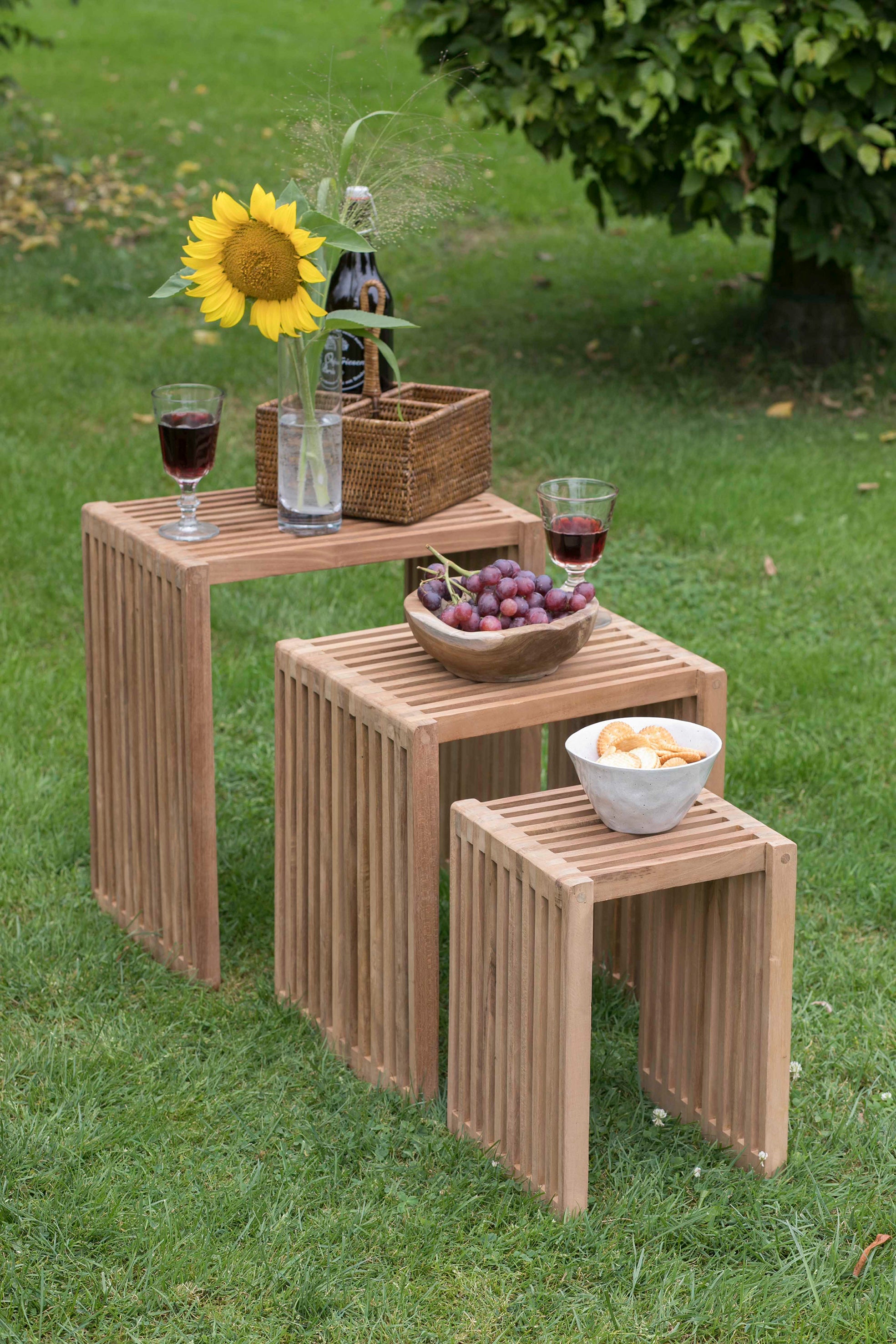 Drei Beistelltische mit Wein, einer Sonnenblume, Weintrauben und Snacks sind auf der grünen Wiese im Freien arrangiert.