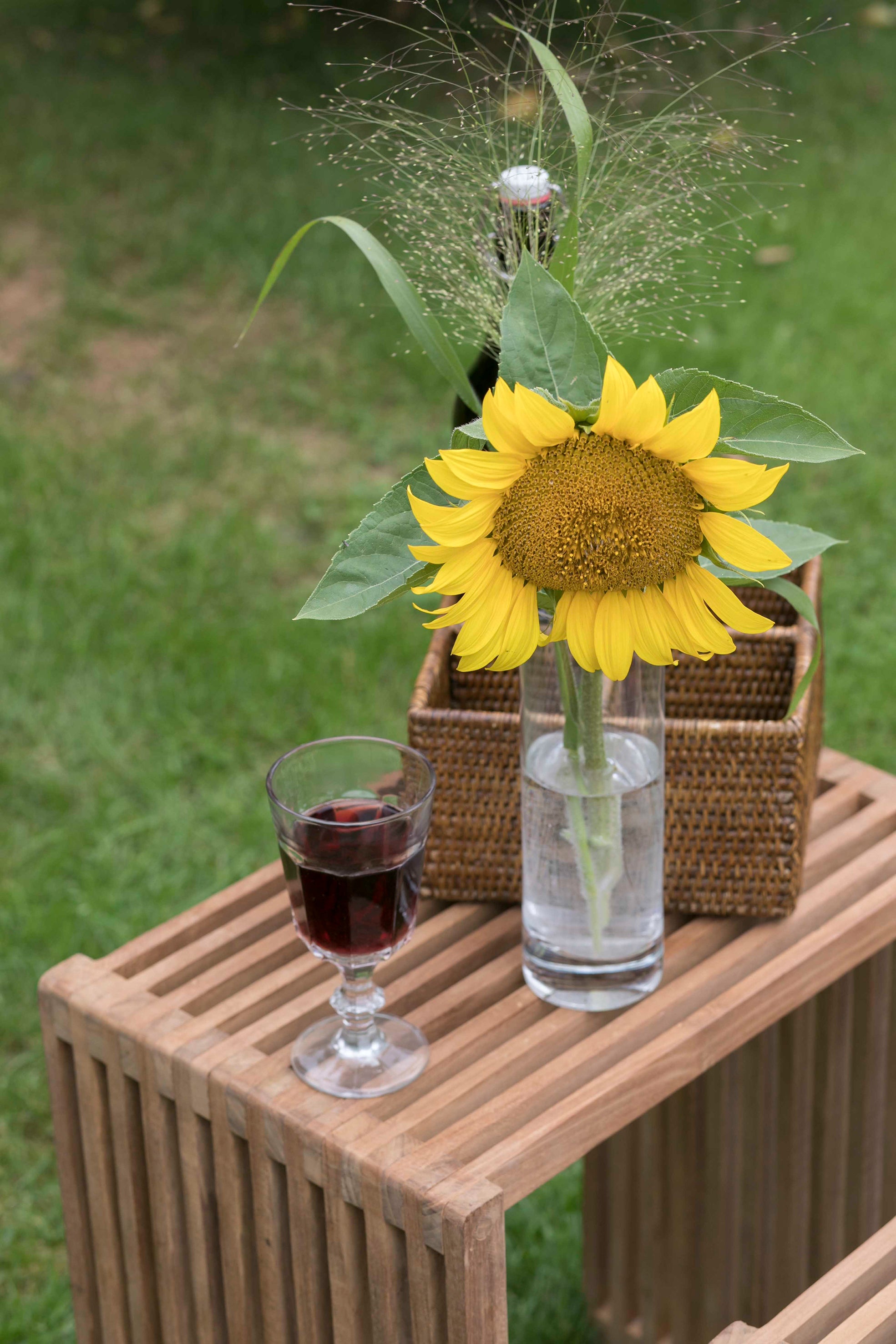 Eine Sonnenblume in einer Vase und ein Glas Rotwein ruhen auf einem Beistelltisch-3er-Set im Freien, platziert auf grünem Gras.