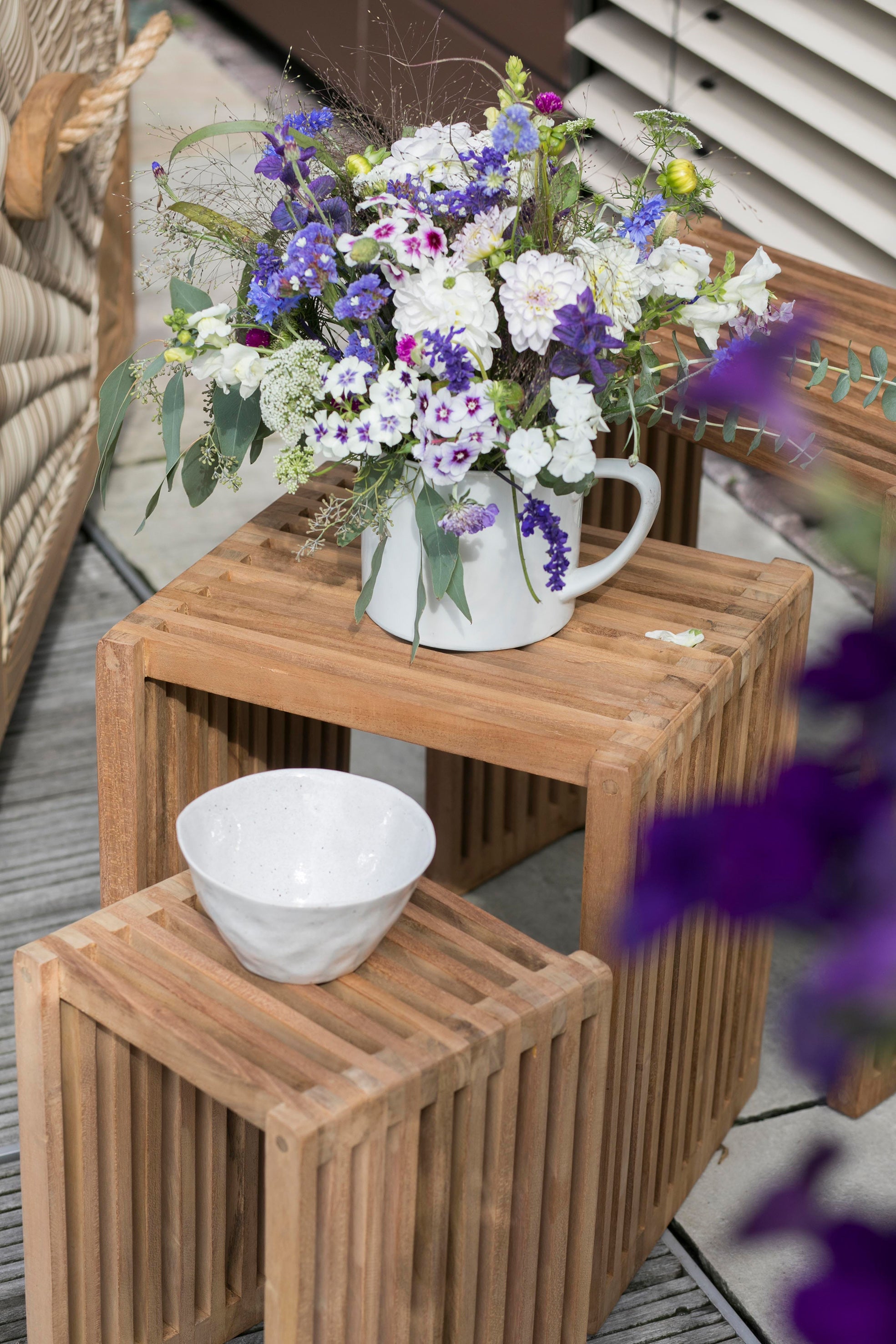 Auf dem Beistelltische-3er-Set steht neben einer weißen Schüssel ein weißer Krug mit violetten und weißen Blumen.