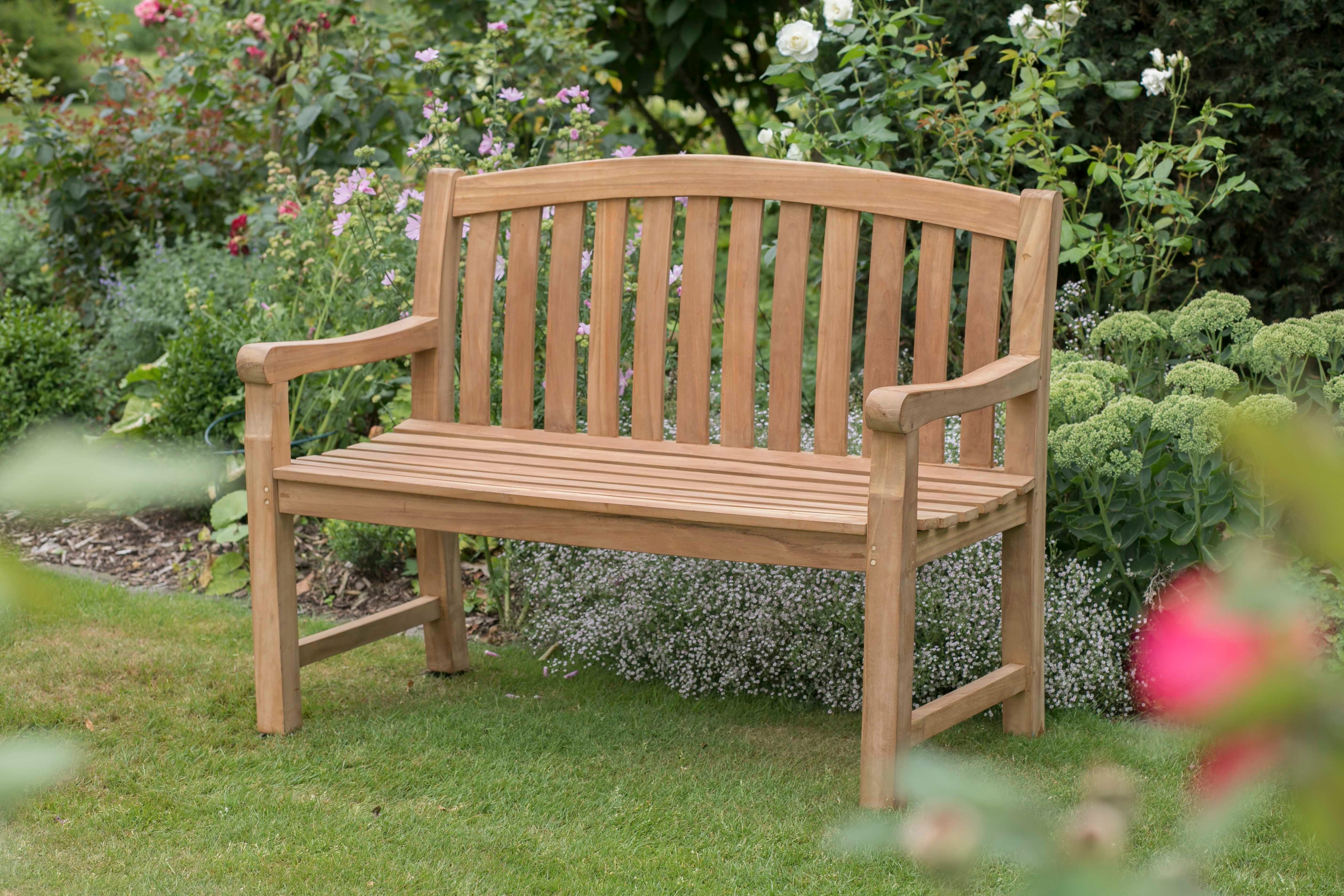 Die Gartenbank Swindon mit ergonomischer Form steht auf dem Rasen, umgeben von grünen Pflanzen und blühenden Blumen.