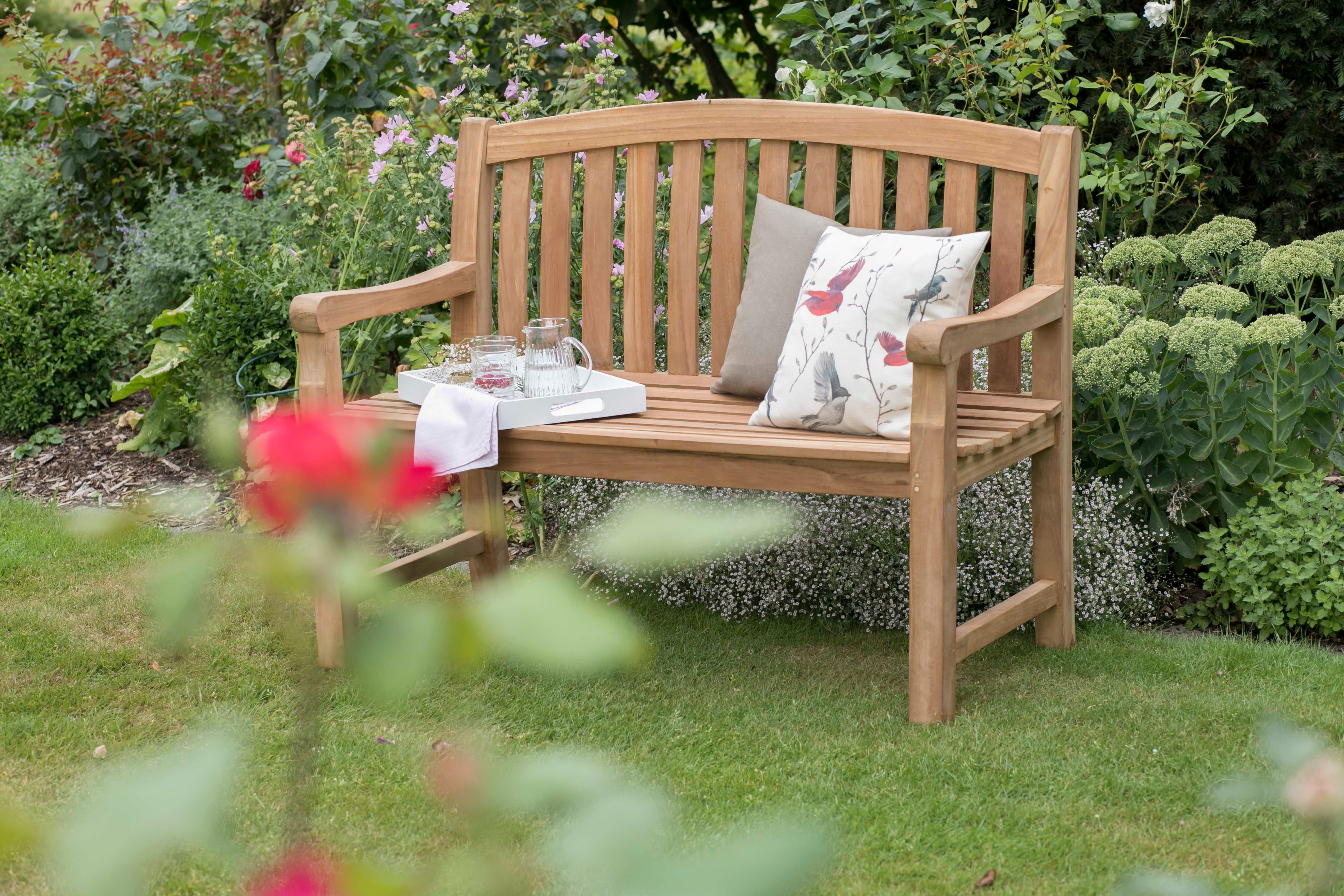 Die Gartenbank Swindon besticht durch ergonomische Form, bequeme Polster und praktische Ablage, eingebettet in üppiges Grün und Blumen.