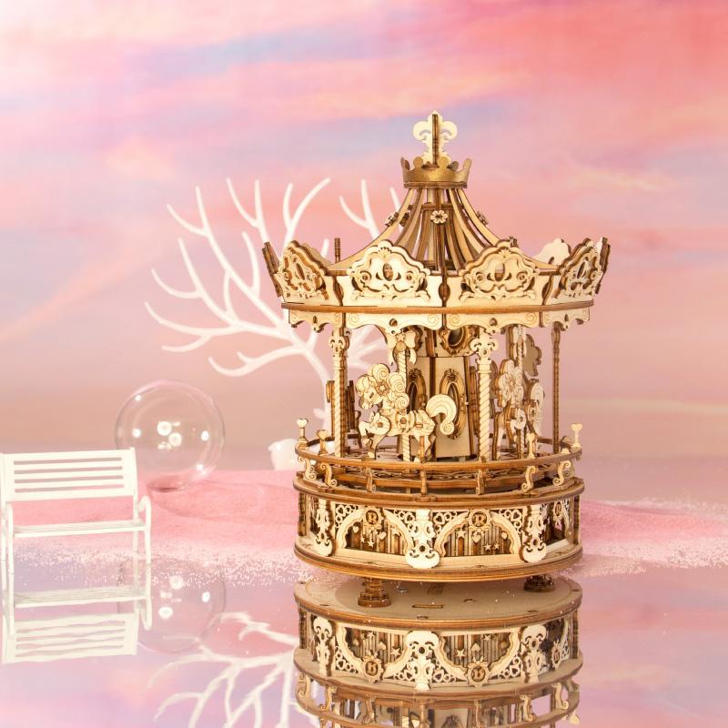 Ein 3D-Holzpuzzle Karussell mit Musikwerk steht auf einer spiegelnden Fläche vor rosa Hintergrund und weißer Bank – ein bezauberndes, bewegliches Bastelprojekt, ideal als persönliches Geschenk.