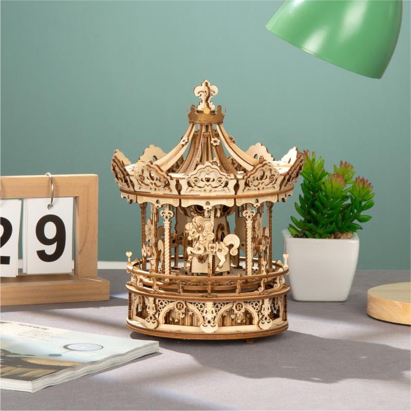 Ein 3D-Holzpuzzle Karussell, beweglich mit Musikwerk, steht auf dem Schreibtisch neben Kalender, Magazin, Lampe und Pflanze – ein ideales Bastelprojekt oder Geschenk für jede kreative Umgebung.