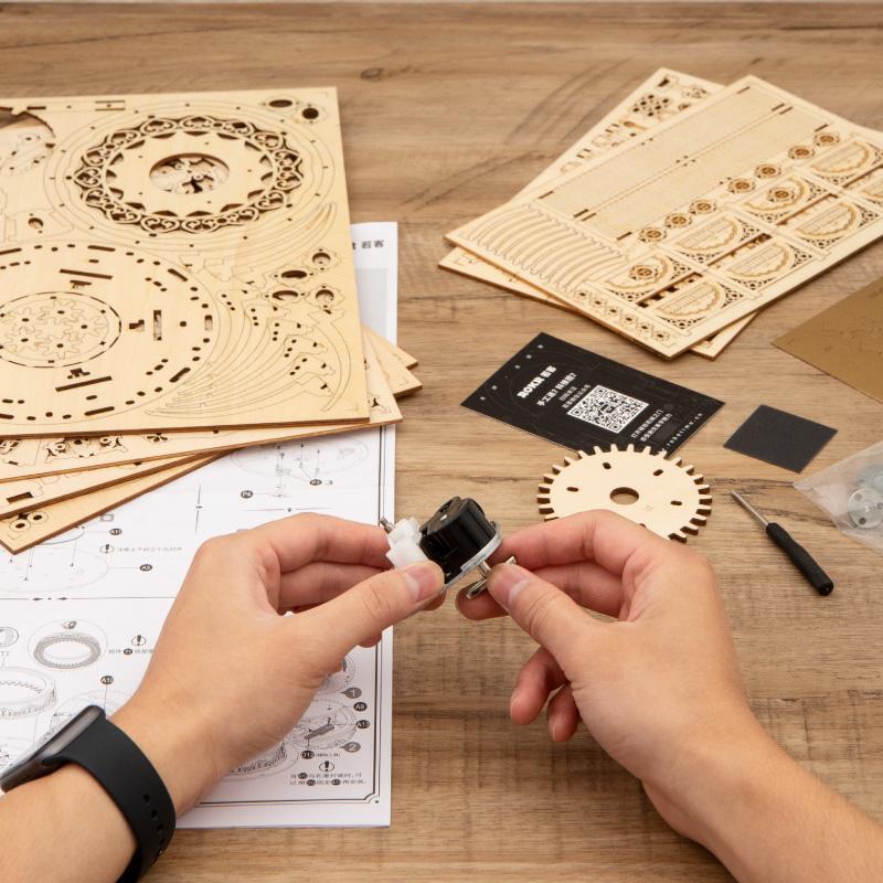 Hände bauen ein 3D-Holzpuzzle „Karussell, beweglich, mit Musikwerk“ auf einem Tisch zusammen – Teile, Werkzeug und Anleitung liegen bereit. Perfekt als Bastelprojekt oder außergewöhnliches Geschenk.