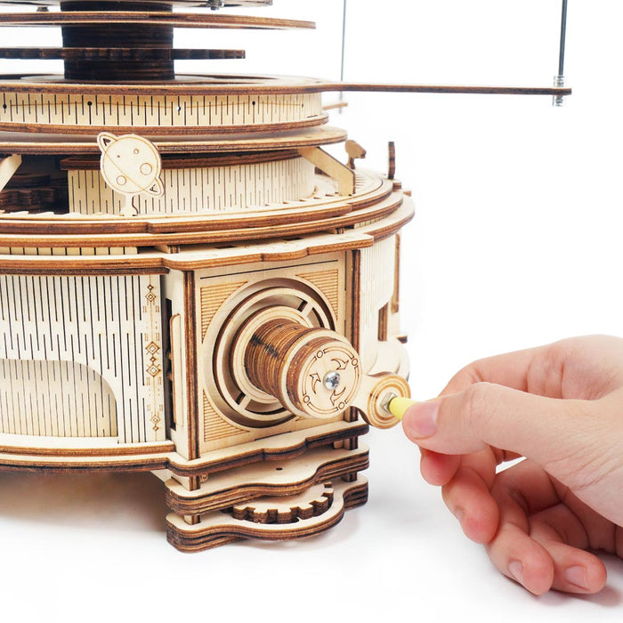 Eine Hand dreht eine Holzkurbel am 3D-Holzpuzzle „Sonnensystem“ – einem komplizierten mechanischen Modell mit detaillierten zahnradähnlichen Designs, die von den Wundern unseres Sonnensystems und seiner Planeten inspiriert sind.