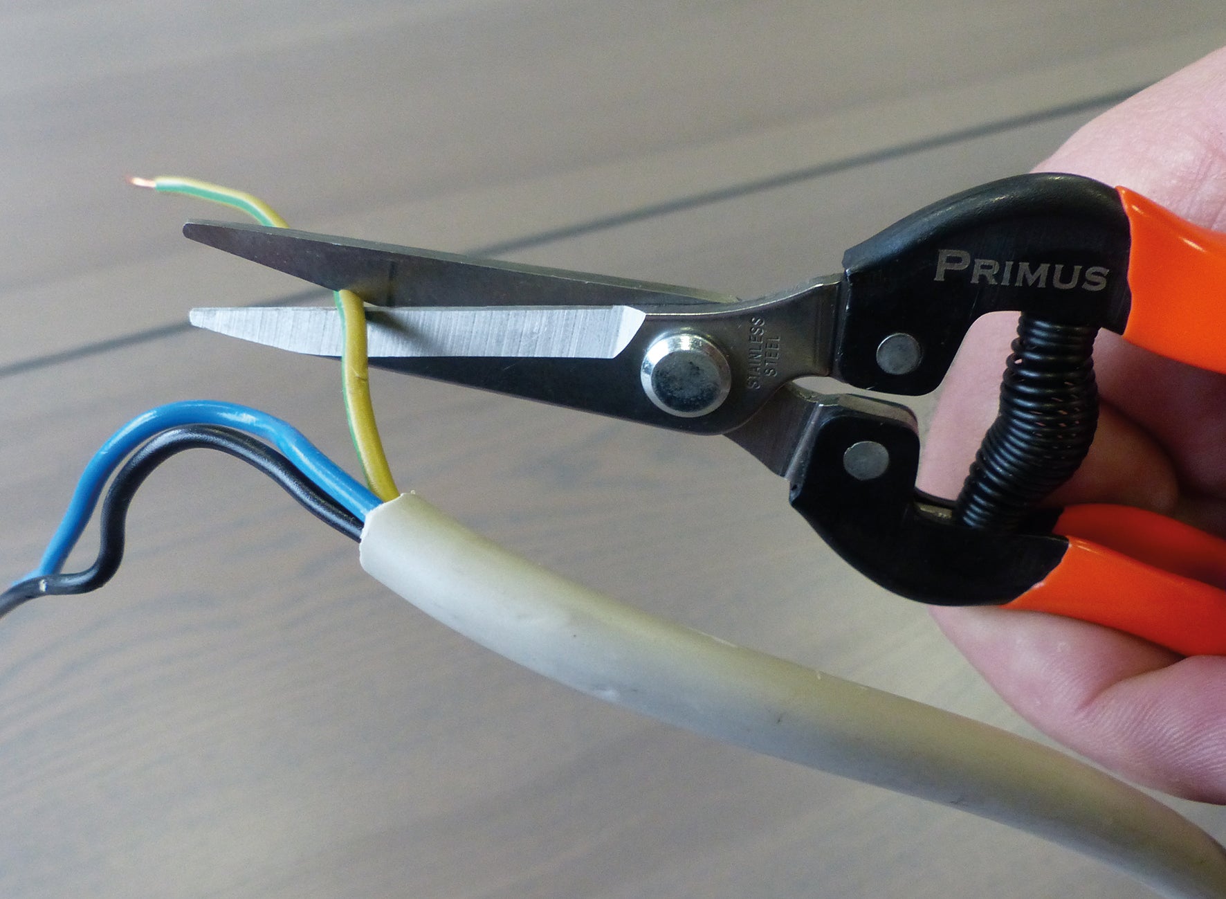 Die Wunderschere – Garten-Schere wird verwendet, um einen gelben Draht in einem Bündel von Elektrokabeln zu durchtrennen; Blaue und grüne Drähte sind ebenfalls sichtbar.