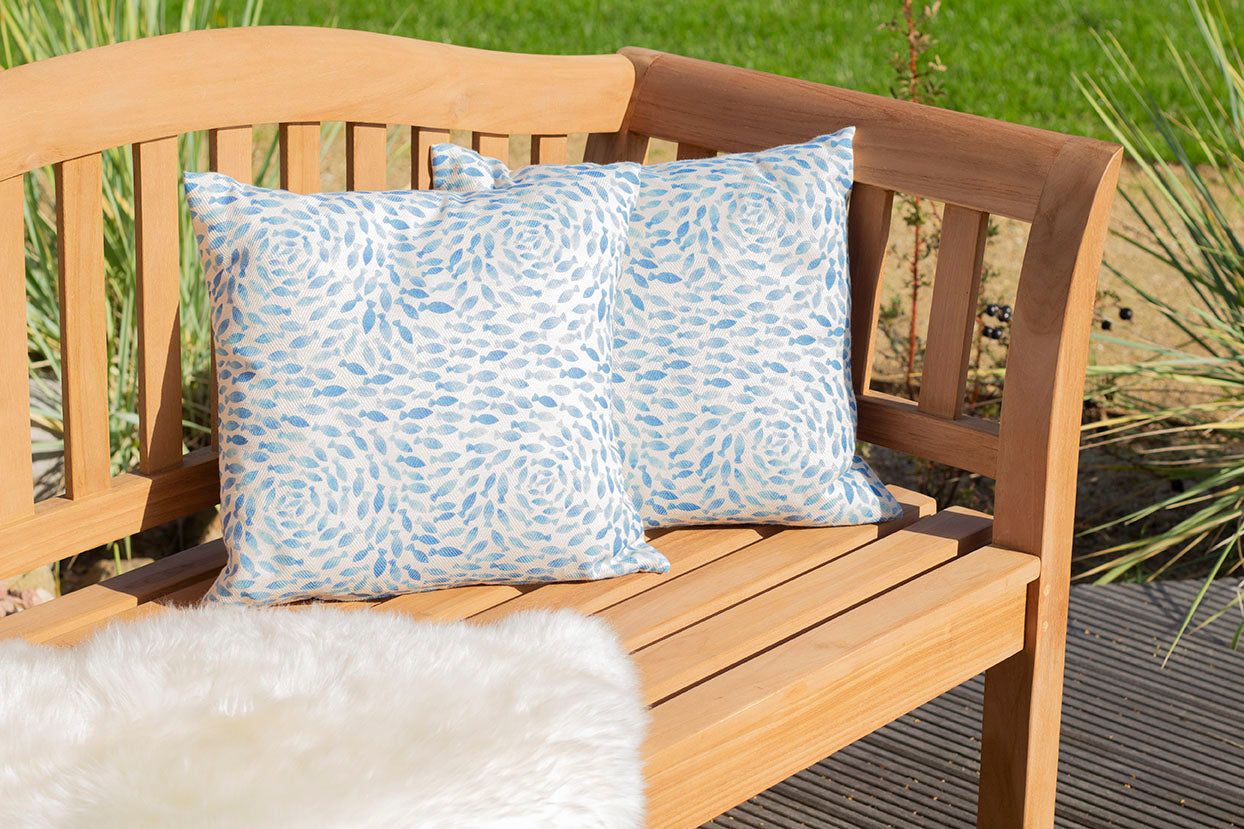 Auf der Gartenbank Wave im Außenbereich liegen zwei gemusterte blau-weiße Kissen, gepaart mit einer kuscheligen Felldecke – eine einladende Note für Ihr Outdoor-Möbel-Ensemble.