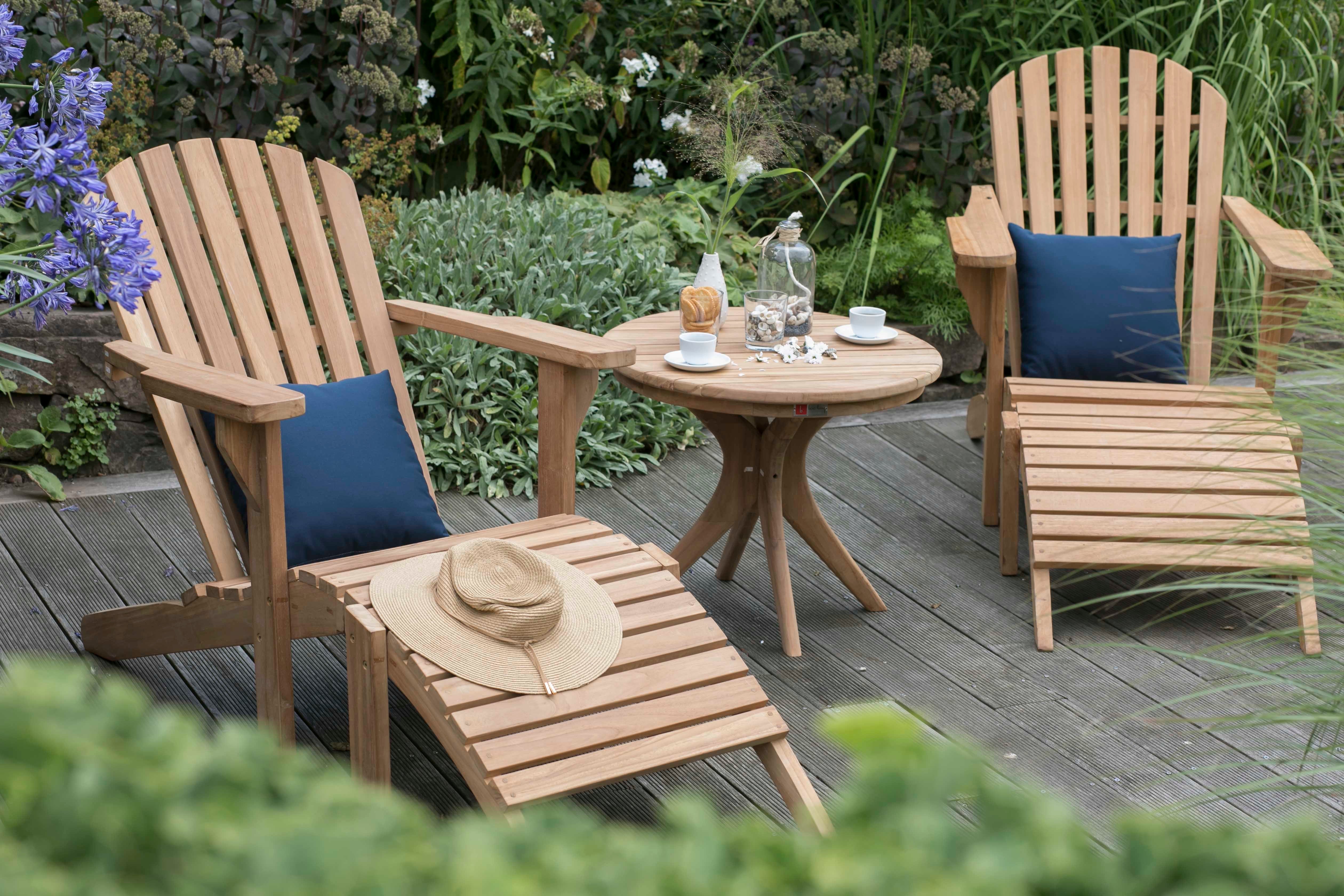 Zwei langlebige Gartenlounger Adirondack Montreal und ein runder Tisch stehen im Garten, mit Getränken, Snacks und einer Hütte – stilvoll und wetterfest für entspannte Stunden im Freien.