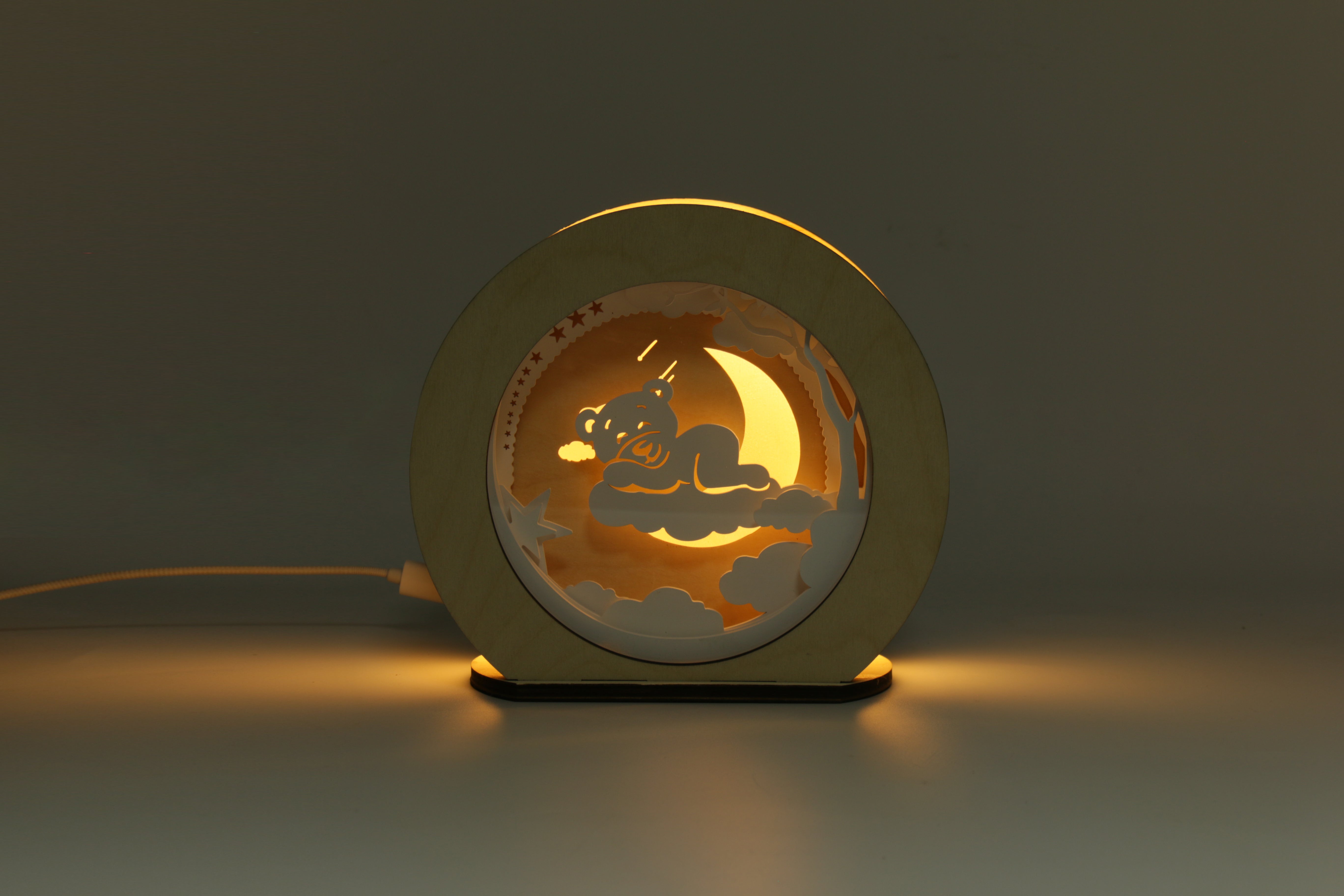 Die Magic Light 3D Holz-Nachtlampe Wolkenbär zeigt einen Bären, der auf einer Mondsichel schläft und im Dunkeln sanft mit moderner LED-Technologie leuchtet, um eine beruhigende Atmosphäre zu schaffen.