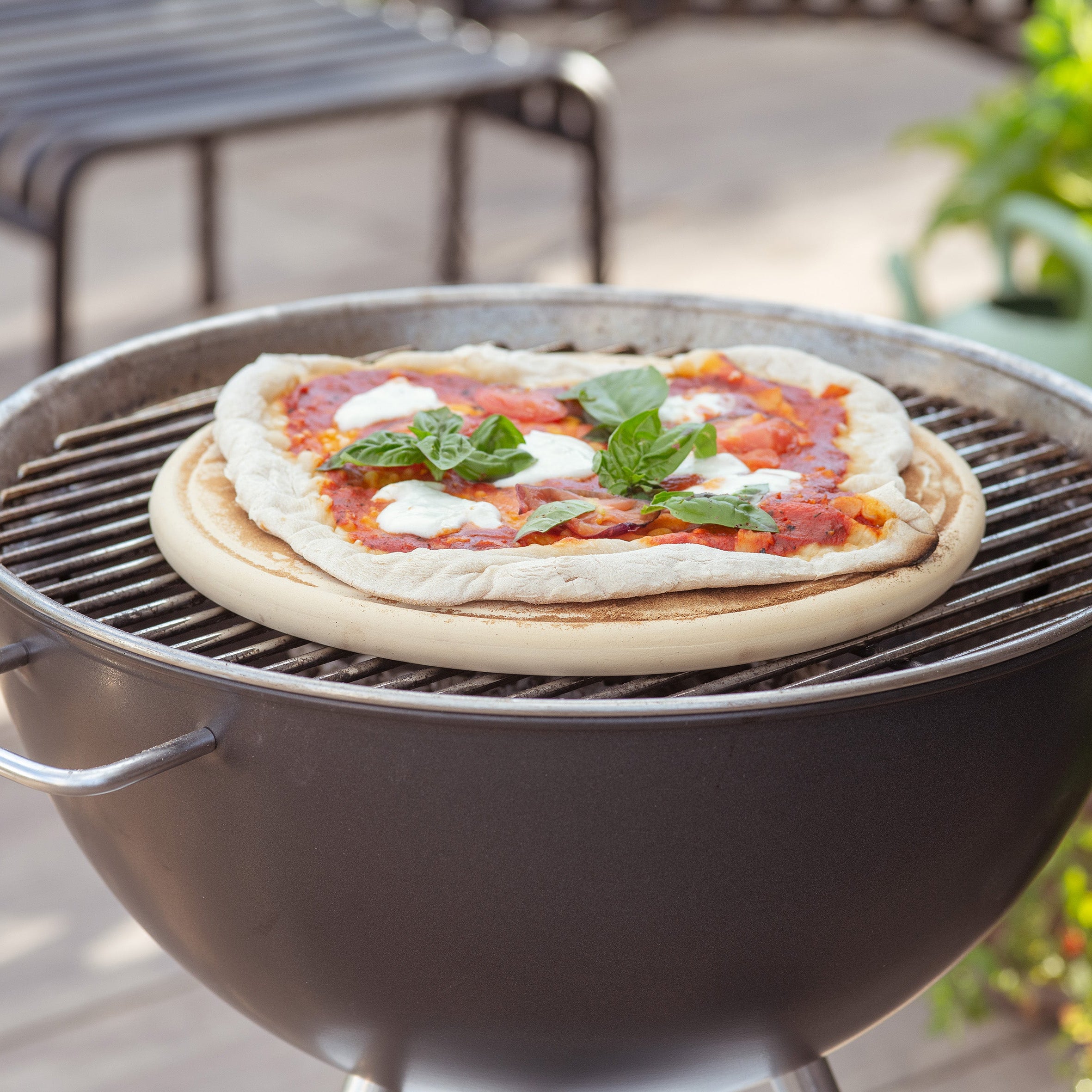 Die Pizzaplatte von DENK Keramik mit einer Pizza auf dem Kugelgrill im Garten