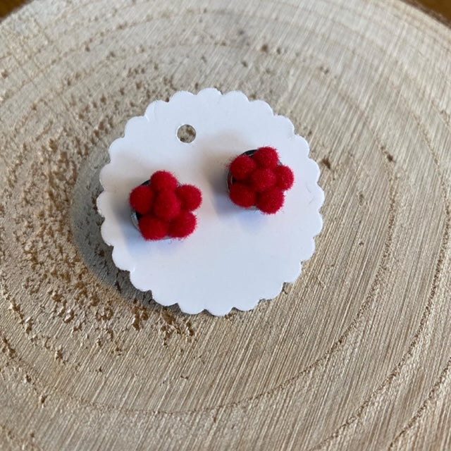 Bollenhut-Ohrringe – rote, flauschige Ohrringe, inspiriert von der Schwarzwälder Tradition, präsentiert auf einer gewellten weißen Karte auf einer Holzoberfläche.