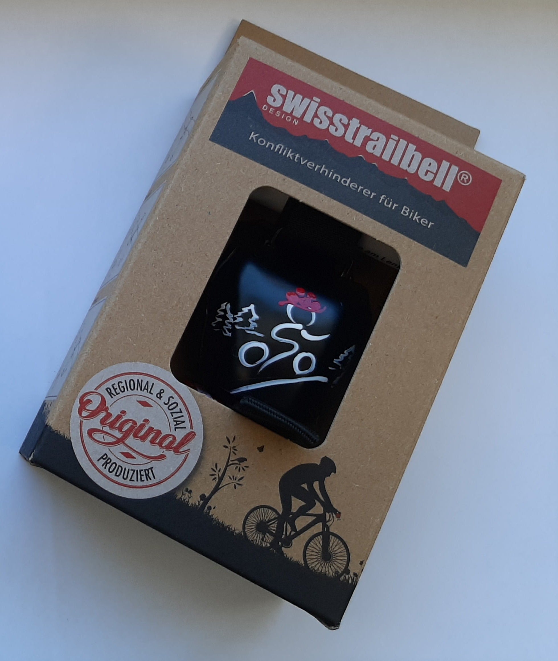 Die Fahrradglocke swisstrailbell® kommt in Verpackung mit Radfahrer-Design und Label „Original Regional & Lokal Produziert“ – sie steht für hochwertige Schweizer Handarbeit.