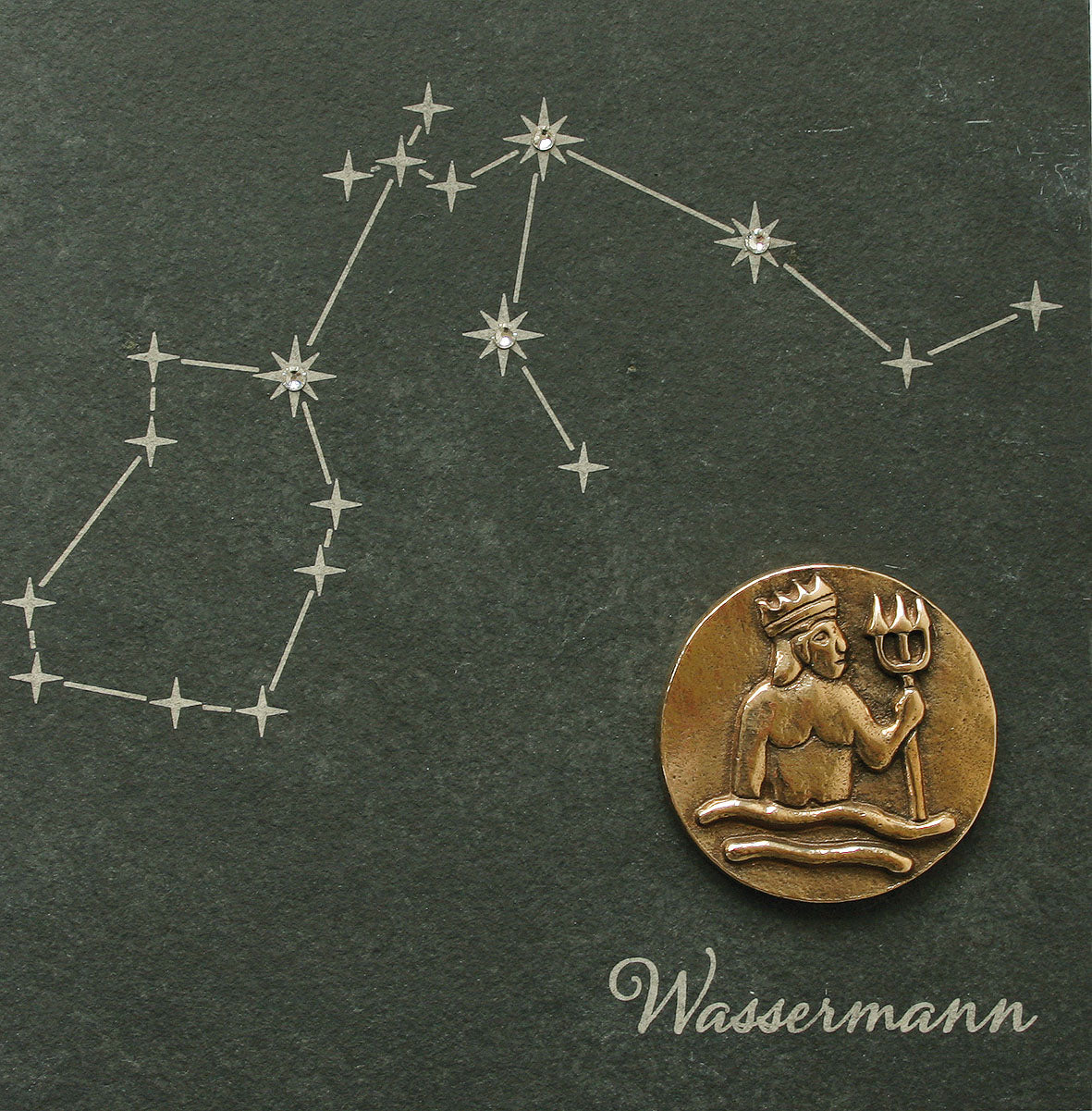Das bronzene Sternzeichen zeigt auf einem Naturschiefer ein Wassermannsymbol und ein Sternbild, akzentuiert mit Swarovski-Elementen, und darunter auf dunklem Hintergrund die Aufschrift „Wassermann“.
