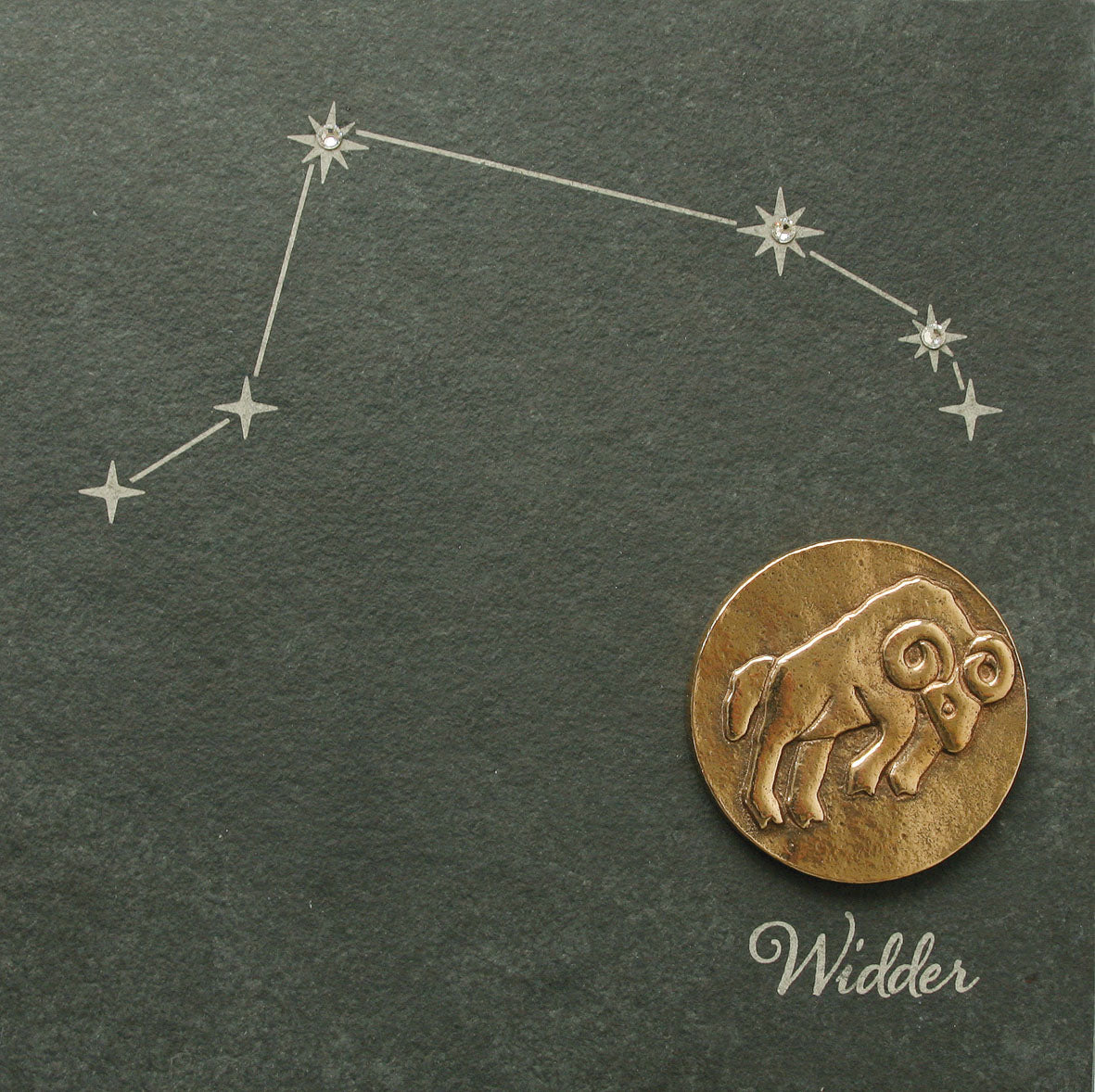 Bronzene Sternzeichenmünze mit dem Widdersymbol mit Swarovski-Elementen und dem Sternbild Widder, vor einem dunklen Naturschiefer-Hintergrund und mit der Aufschrift „Widder“.