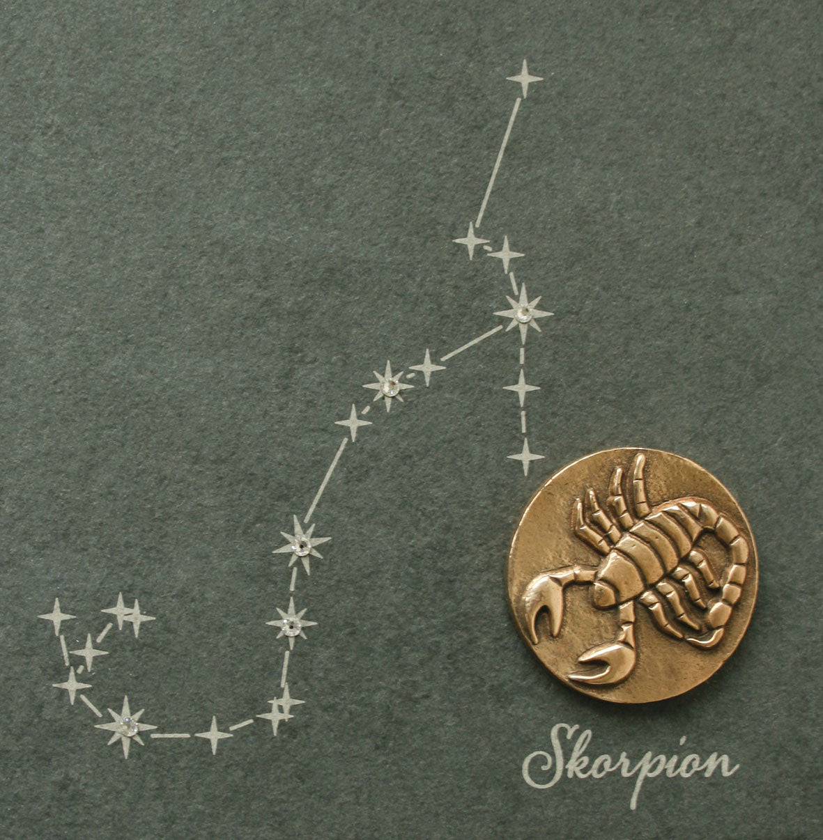 Das Bronze-Sternzeichen zeigt ein Skorpion-Medaillon mit Swarovski-Elementen neben dem Sternbild Skorpion auf dunklem Naturschiefer.