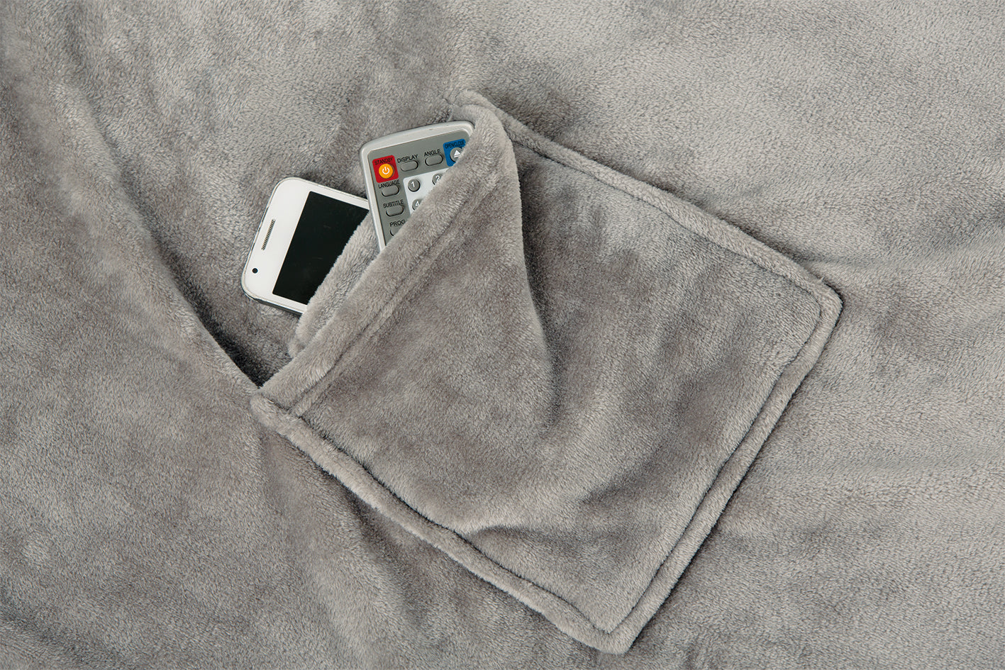 Ein weißes Smartphone und eine TV-Fernbedienung in der Tasche einer weichen grauen Ärmeldecke.