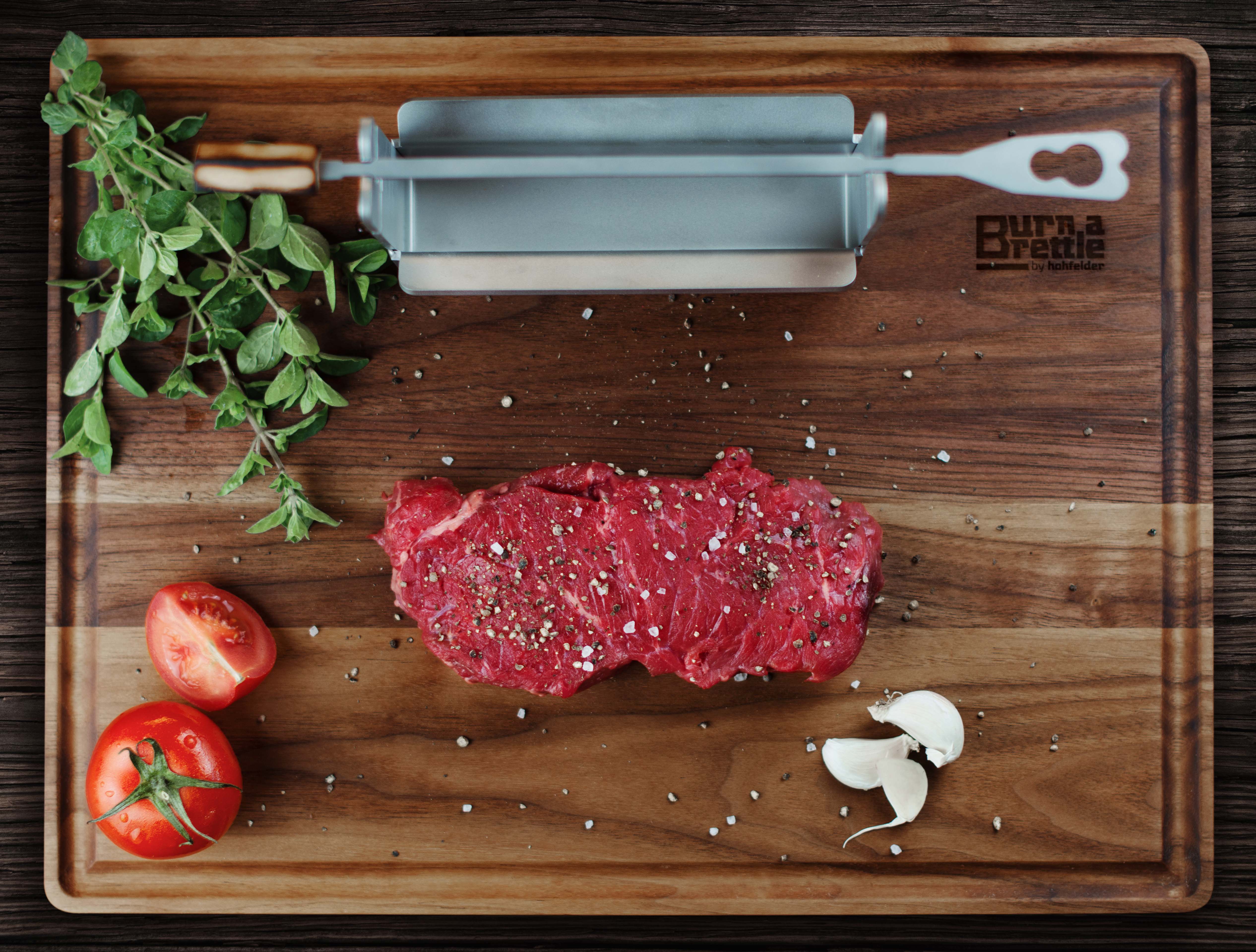 Ein Brettle anbrennen: Rohes Steak mit Paprika, Tomaten, Knoblauch und Kräutern auf einem Holzschneidebrett mit einem Edelstahlschneider – die perfekte Grill-Idee mit nachhaltigen Materialien.