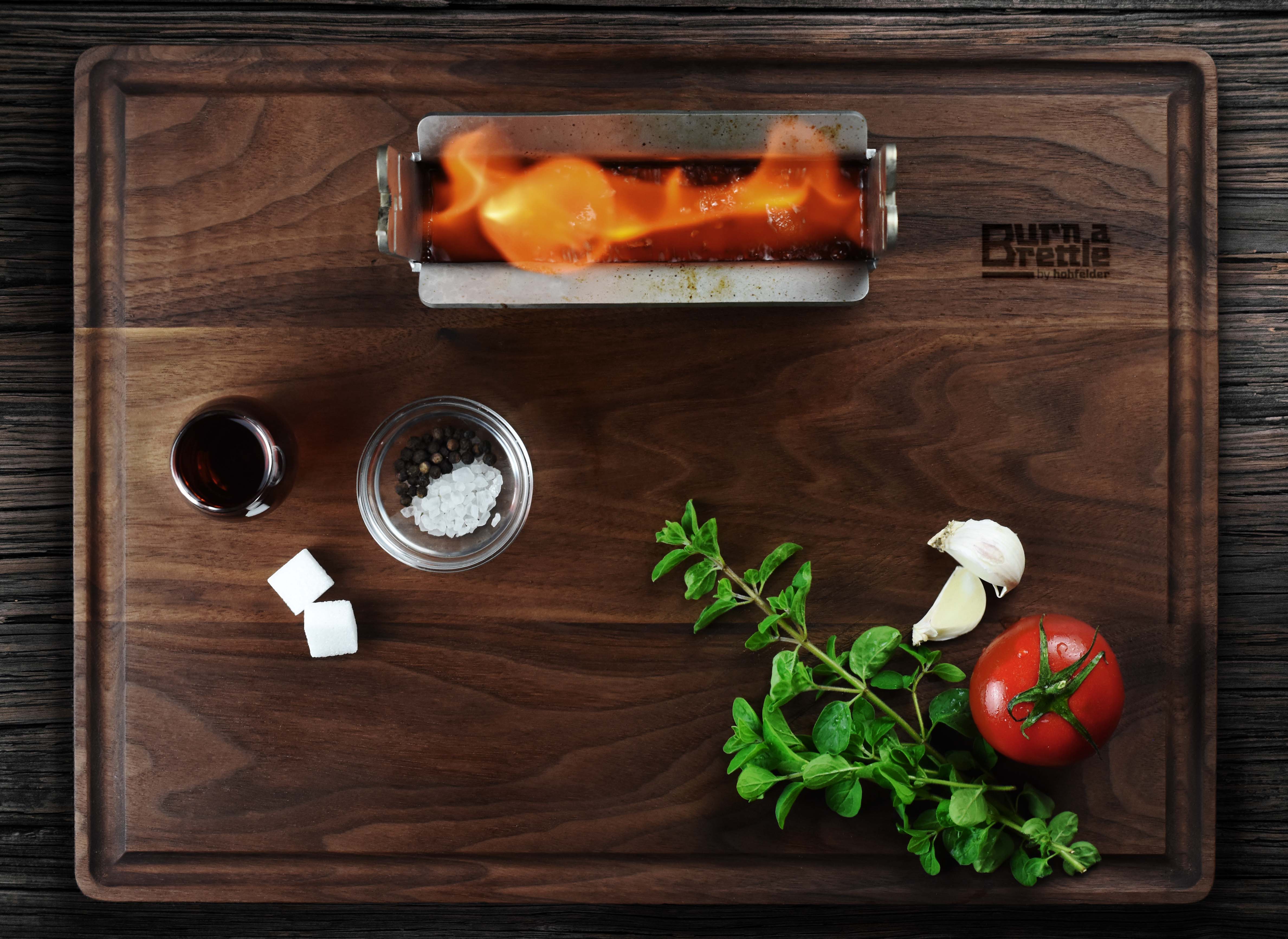 Burn a Brettle: nachhaltiges Holzbrett mit Burner Flame, Kräutern, Tomate, Knoblauch, Pfeffer, Salz, Zuckerwürfeln und einem Glas – eine inspirierende Grill-Idee für bewusste Genießer.