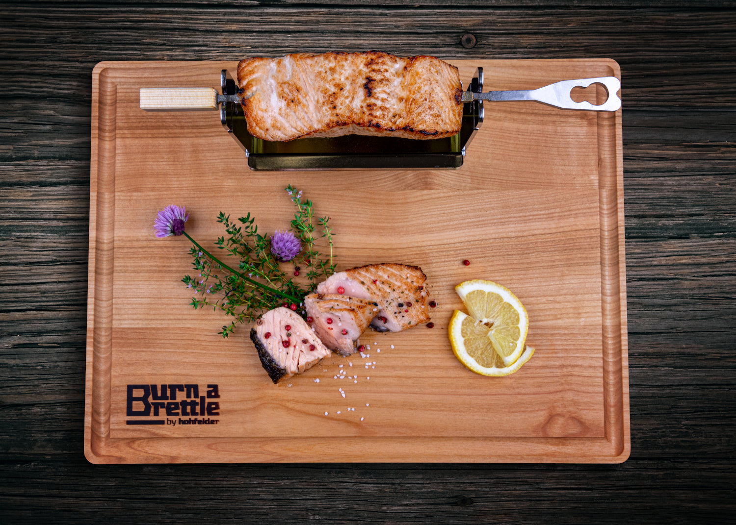 Gegrillter Lachs auf Burn a Brettle mit Zitrone, Kräutern und rosa Pfefferkörnern, dazu ein Fischwender aus Edelstahl – Ihre perfekte Grillidee mit nachhaltigen Materialien.