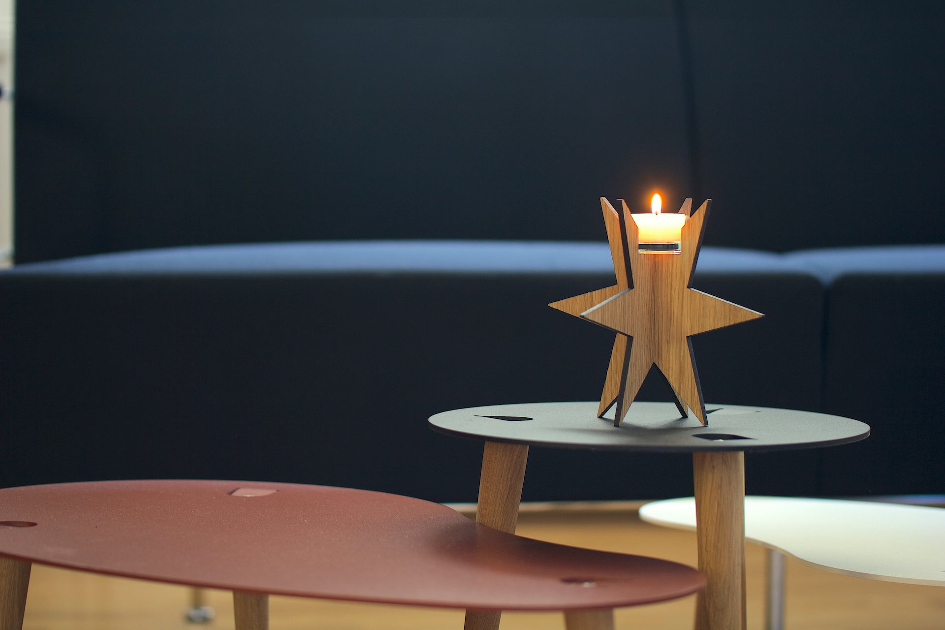 Eine brennende Kerze in einem Teelichthalter Sternenlicht steht auf einem schwarzen Tisch, im Hintergrund sind weitere Tische und ein Sofa zu sehen.