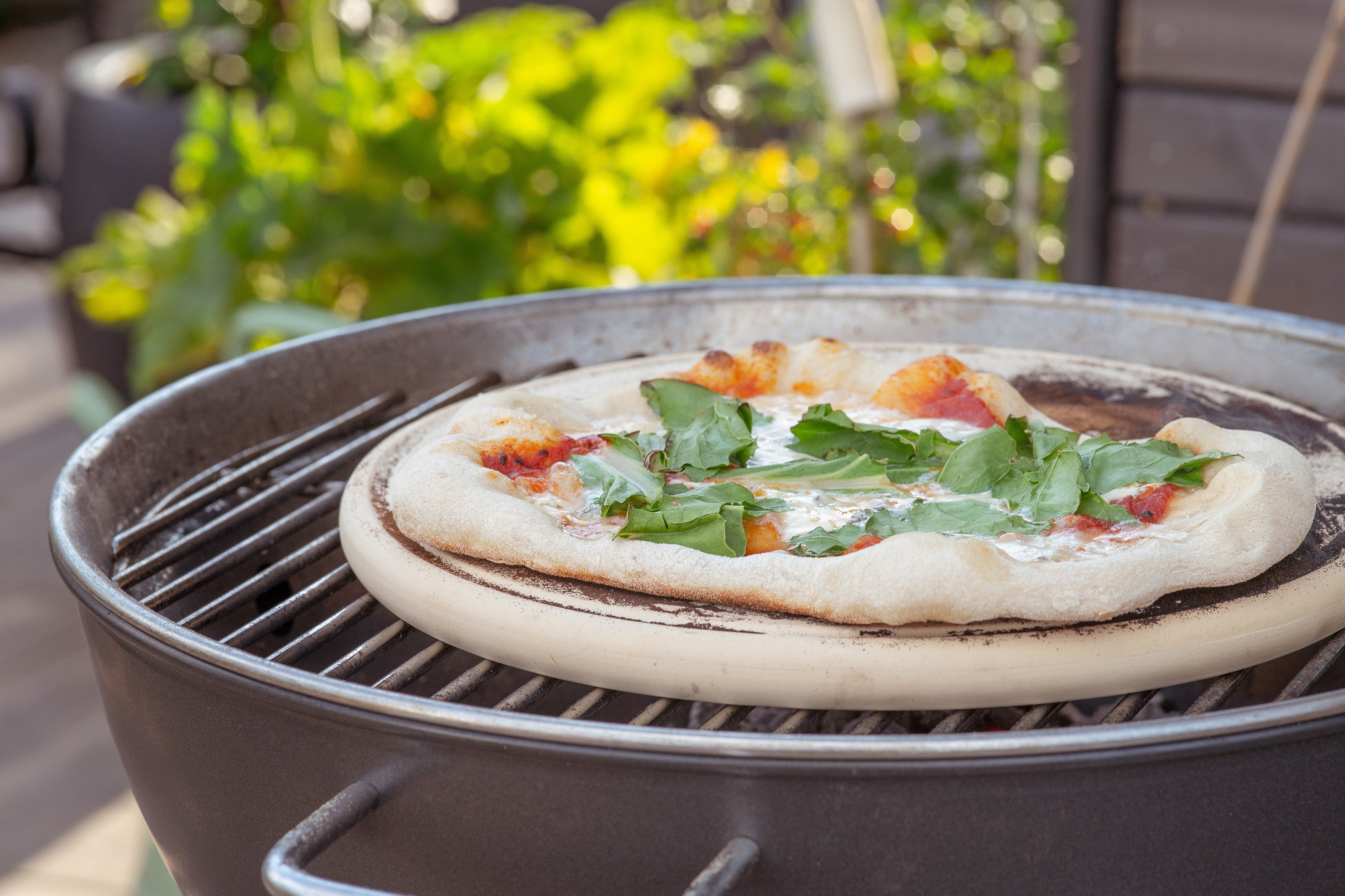 Die Pizzaplatte von DENK Keramik mit einer Pizza auf dem Kugelgrill im Garten
