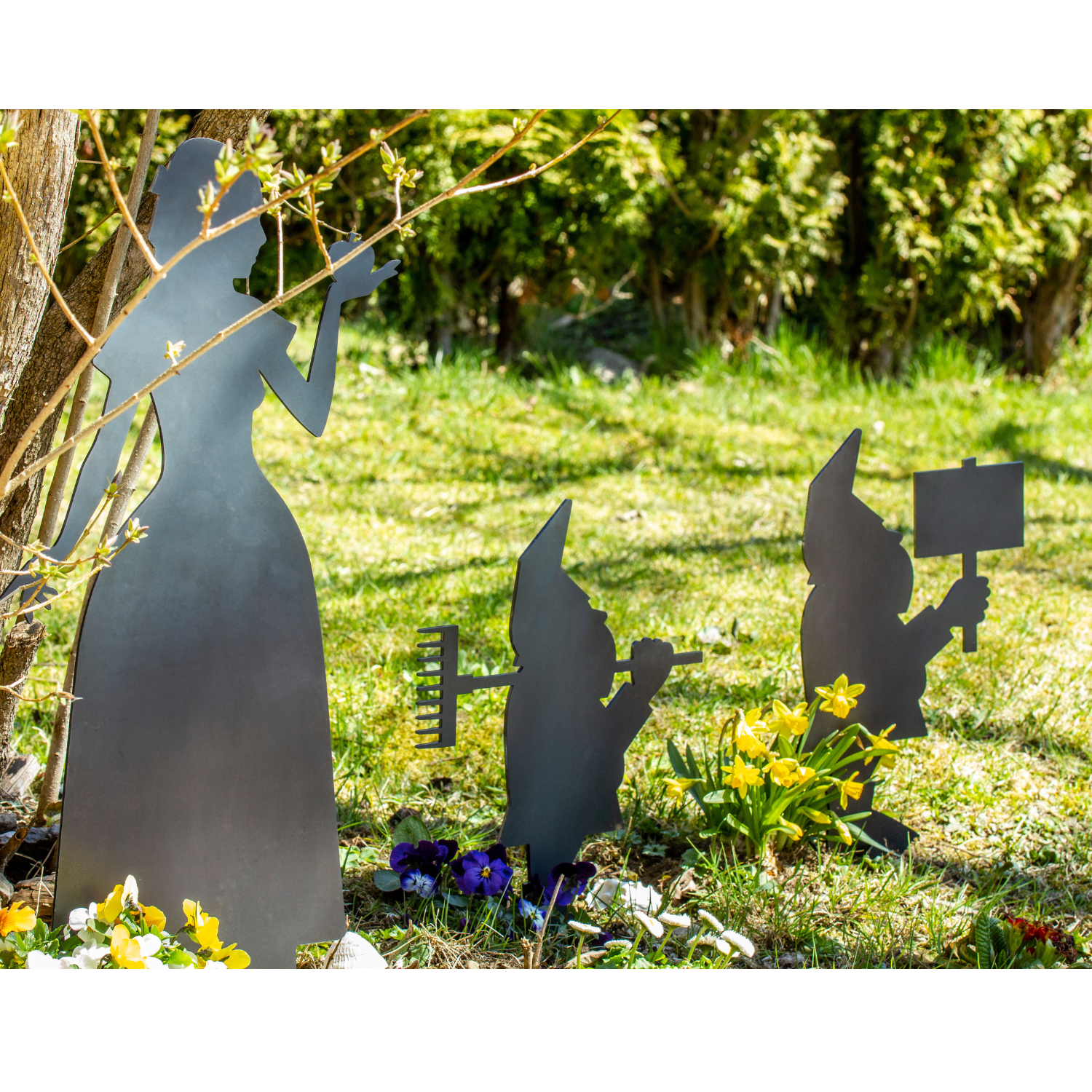 Gartenzwerge aus Stahl stehen zwischen Blumen und Gras im Garten.