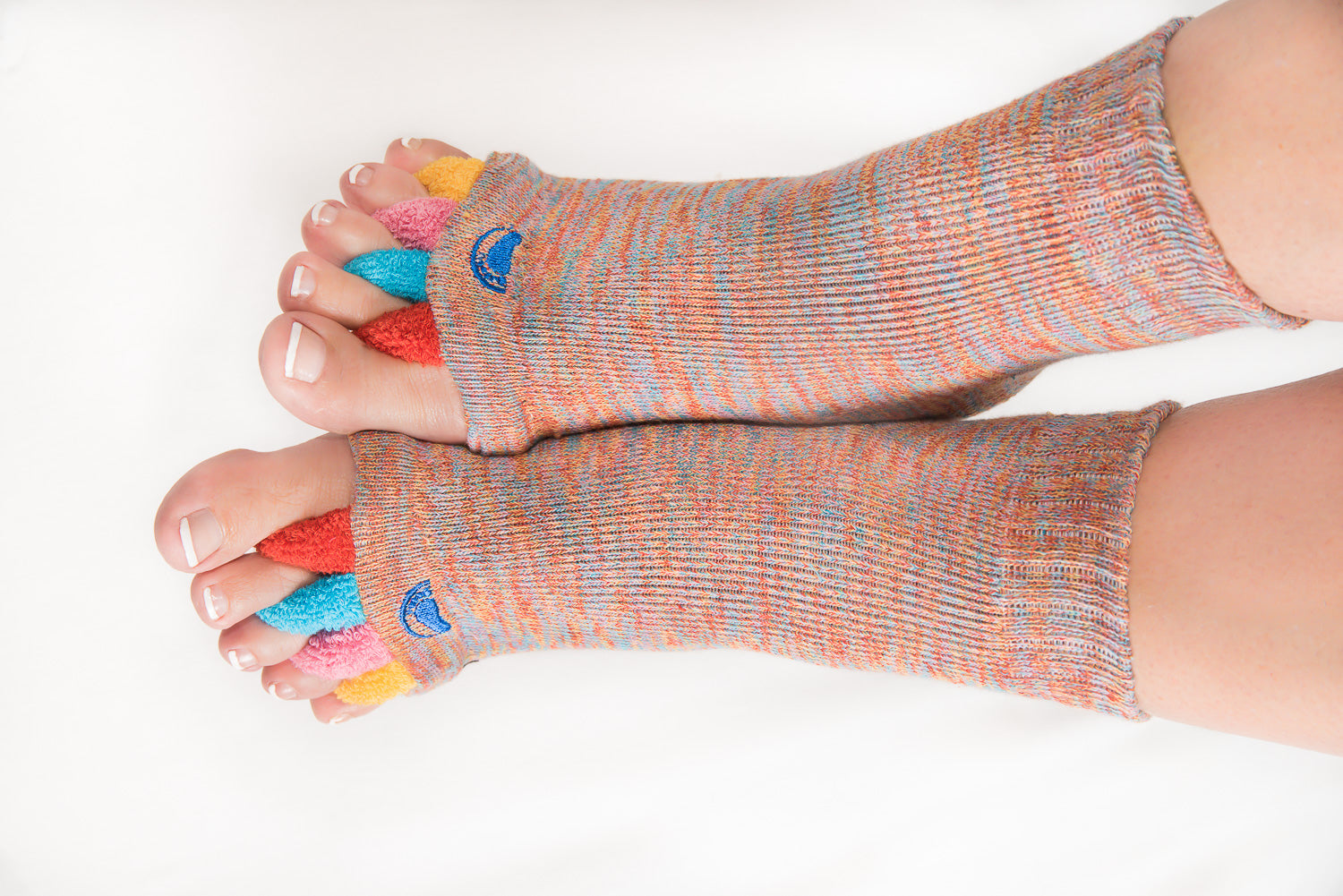 Füße in Fußausrichtungssocken „Happy Feet“ mit buntem Stoff zwischen den Zehen ruhen auf einer weißen Unterlage – perfekt als therapeutisches Hilfsmittel zur Linderung von Fußbeschwerden.