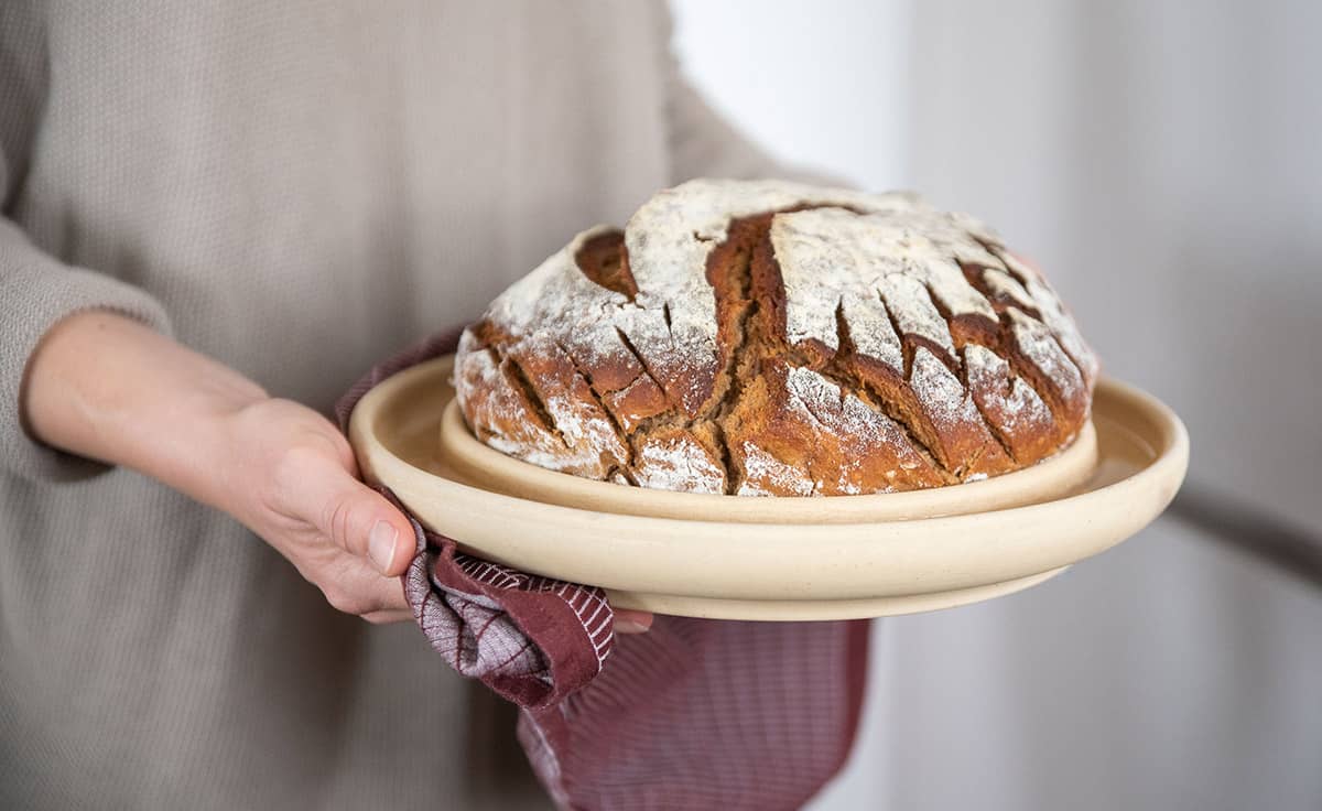 Die Backplatte Bread & Cake von DENK Keramik in den Händen einer Frau mit frisch gebackenem Brot